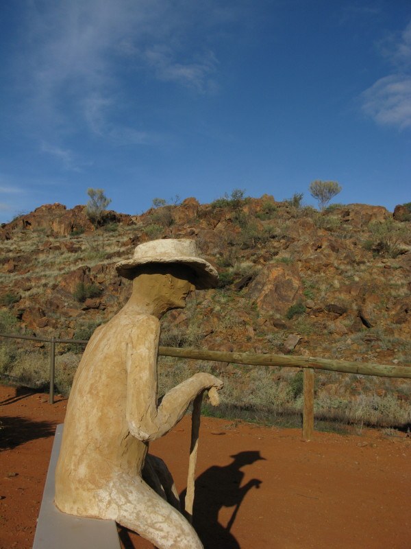 sculpture of man sitting down with hat and cane