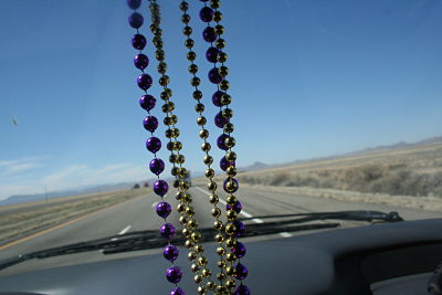 mardi gras beads hanging from the mirror looking out the front window of a van driving on a road